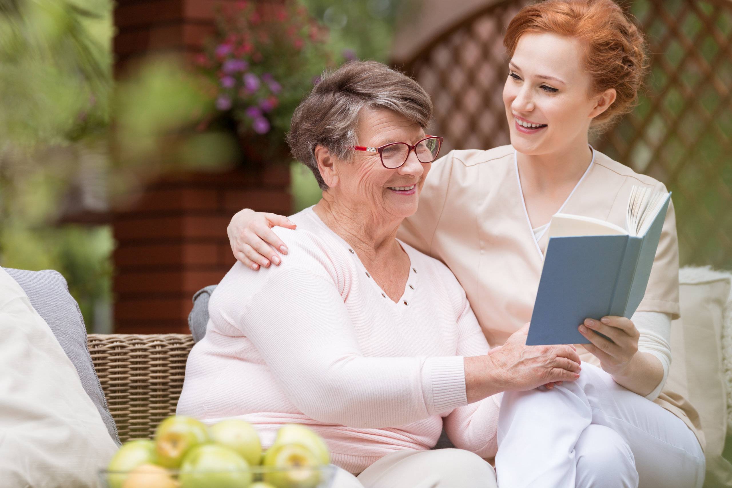 an elderly woman and her caregiver reading a book together outside