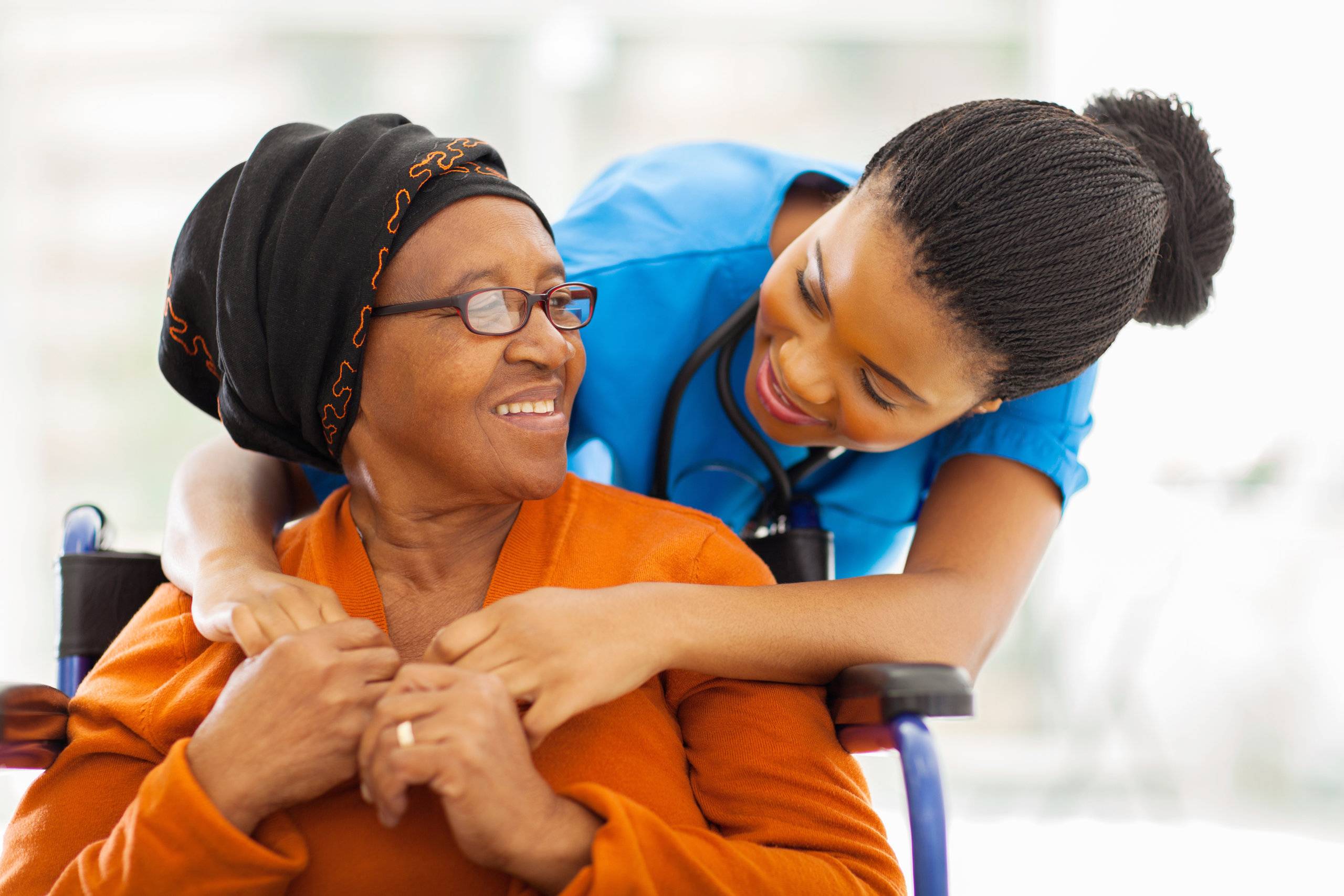 nurse hugging a senior woman on wheelchair